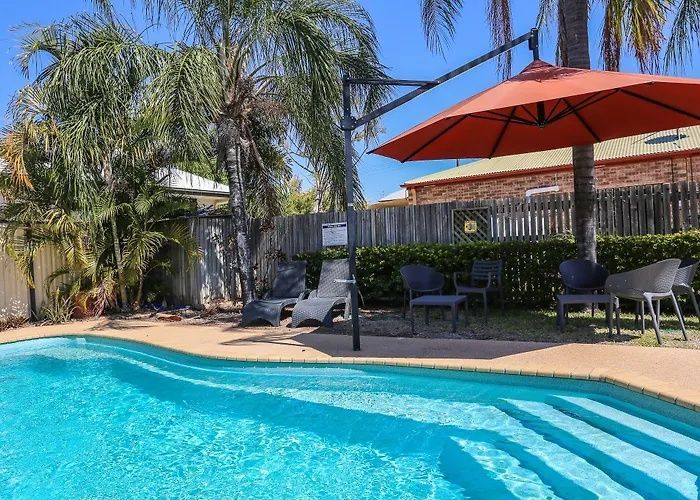 Palm-lined backyard pool with lounge chairs, shade umbrellas, and a sunny patio