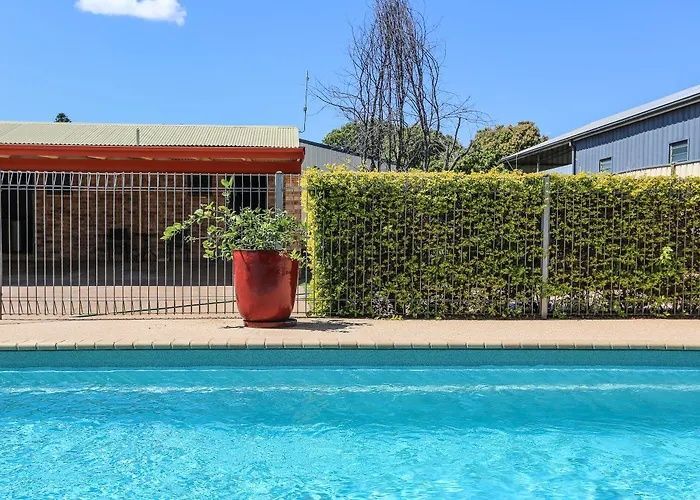 Blue swimming pool with a hedge, red planter, and gated building in the background under a clear sky.