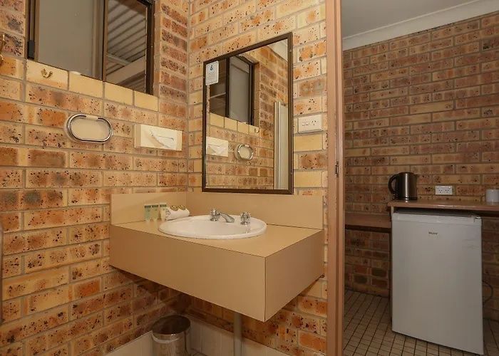 Small brick bathroom with tan sink, mirror, and white mini fridge in the corner.
