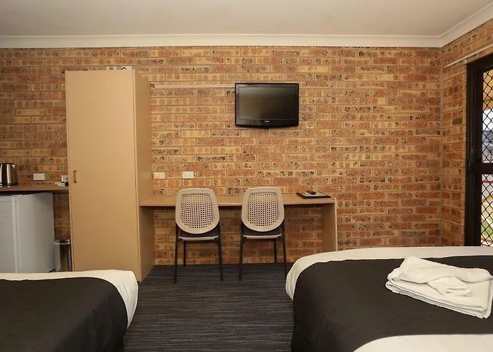 Motel room with two beds, two chairs, a desk, and a wall-mounted TV against a brick wall.