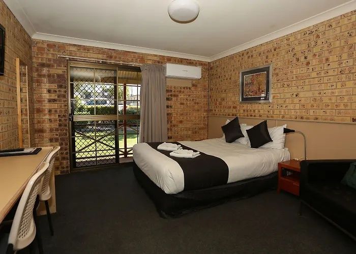Small hotel room with brick walls, double bed, desk, and sliding glass door to a balcony.