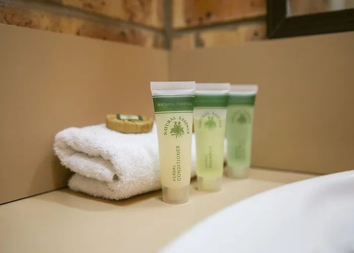 Spa toiletries beside a folded white towel by a bathtub, with green and cream tubes and a soap dish