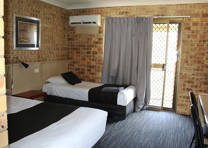 Small hotel room with two beds, brick walls, gray curtains, and a glass door to a balcony