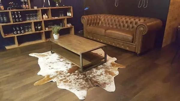 Cozy lounge with a brown leather couch, low wooden table, shelves, and a cowhide rug on the floor.