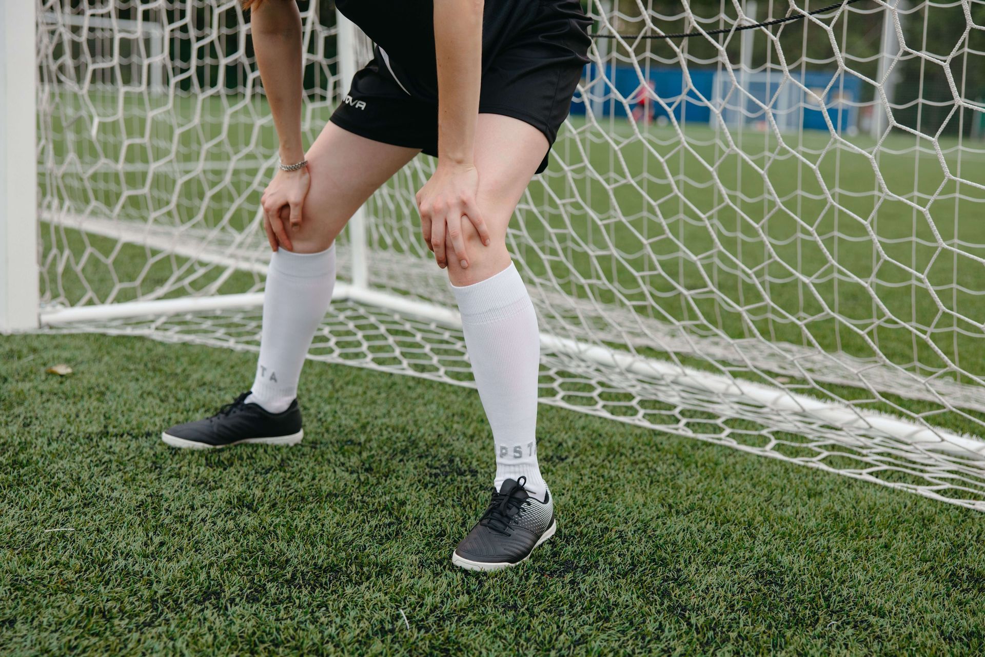 Close-up of a person leaning forward with their hands on their knees on a soccer field, illustrating overwhelm and performance-related stress explored in sports performance anxiety therapy in Omaha, NE | sports performance anxiety therapy omaha ne - anxiety therapy omaha ne - anxiety therapist omaha ne - elkhorn - gretna - bennington - blair - millard - wahoo - waverly - papillion
