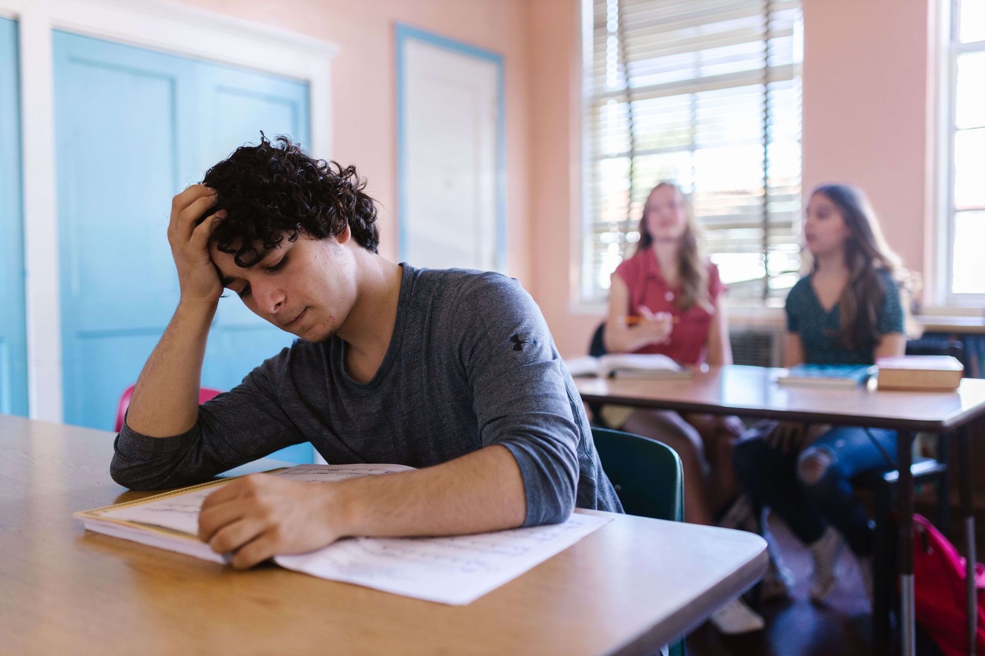 Person sitting in a classroom looking stressed while two classmates talk behind them, representing social anxiety, emotional overwhelm, and challenges addressed through therapy for social anxiety in Omaha, NE | therapy for social anxiety omaha ne - anxiety counseling omaha ne - anxiety therapist omaha ne - elkhorn - gretna - bennington - blair - millard - wahoo - waverly - papillion