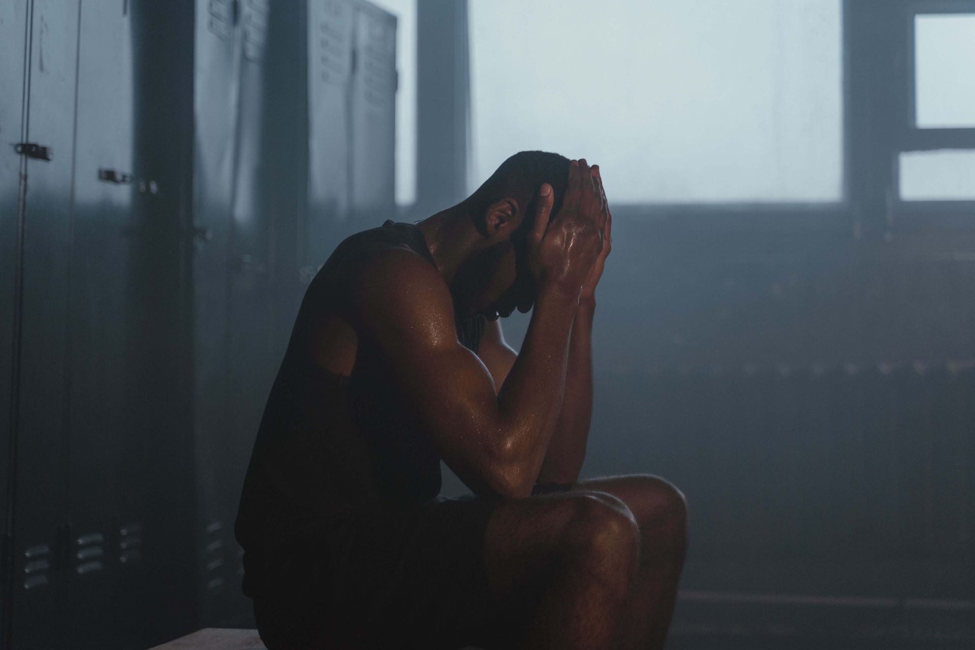 Athlete sitting in a locker room with hands on his head looking distressed, representing the emotional impact of injury, loss, and major changes addressed through grief therapy for athletes in Omaha, NE | grief therapy for athletes omaha ne - therapy for grief and anxiety omaha ne - grief therapy for athletes omaha ne - elkhorn - gretna - bennington - blair - millard - wahoo - waverly - papillion