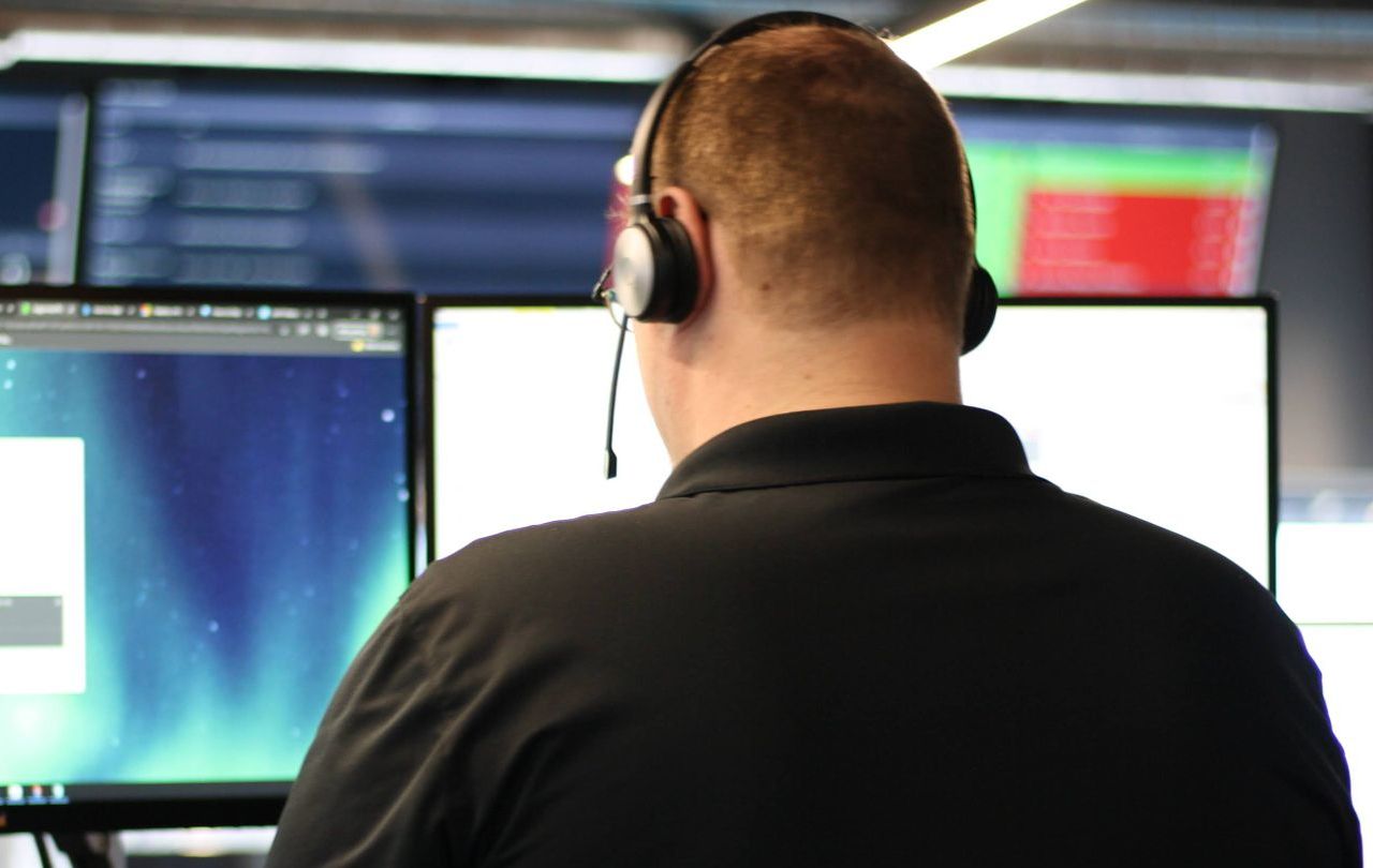 A man wearing headphones sits in front of a computer monitor