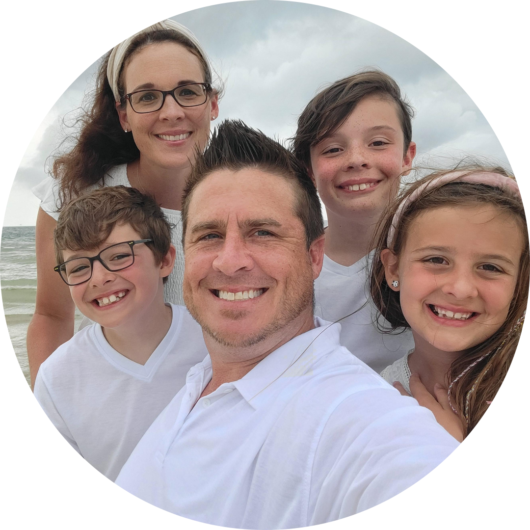 Family selfie on the beach: smiling mother, father, and three children in white clothes.