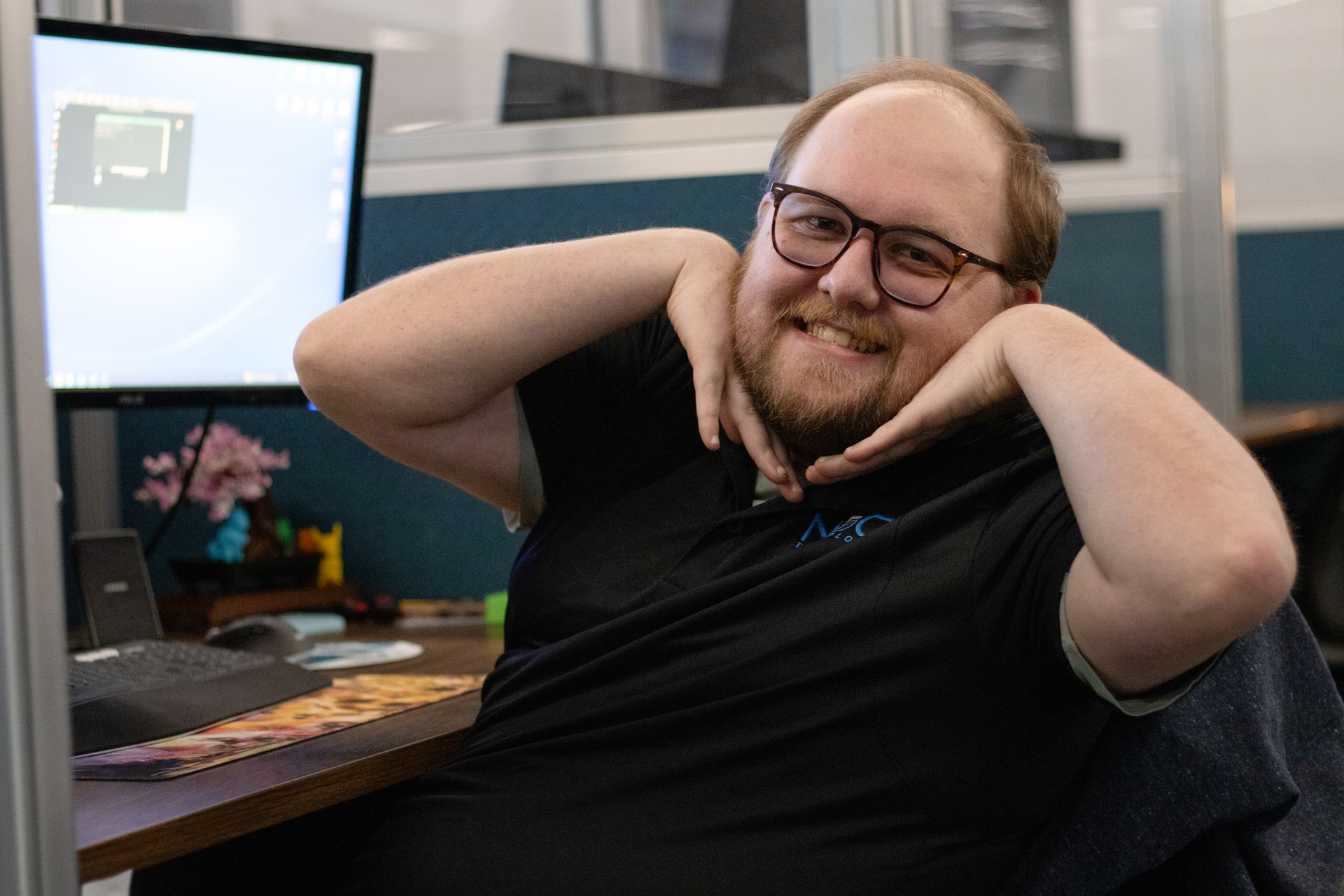 Man with glasses, smiling, hands near face. Sitting at desk, office setting.