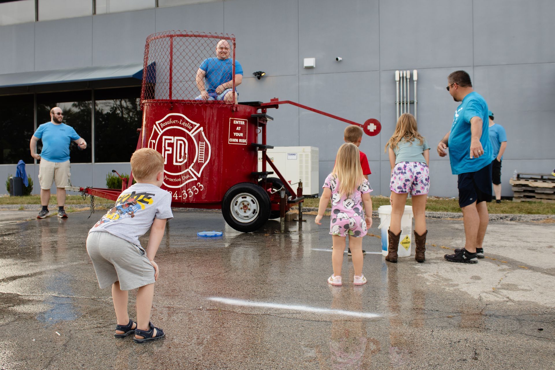 Children and adults playing a red fire truck water game on a wet street at a community event