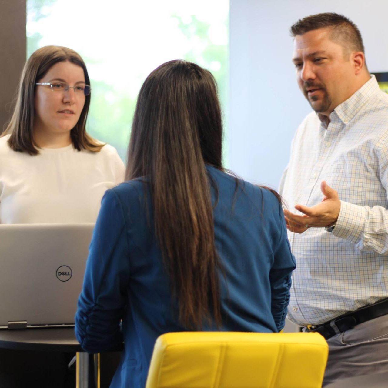 A man is talking to two women in front of a dell laptop