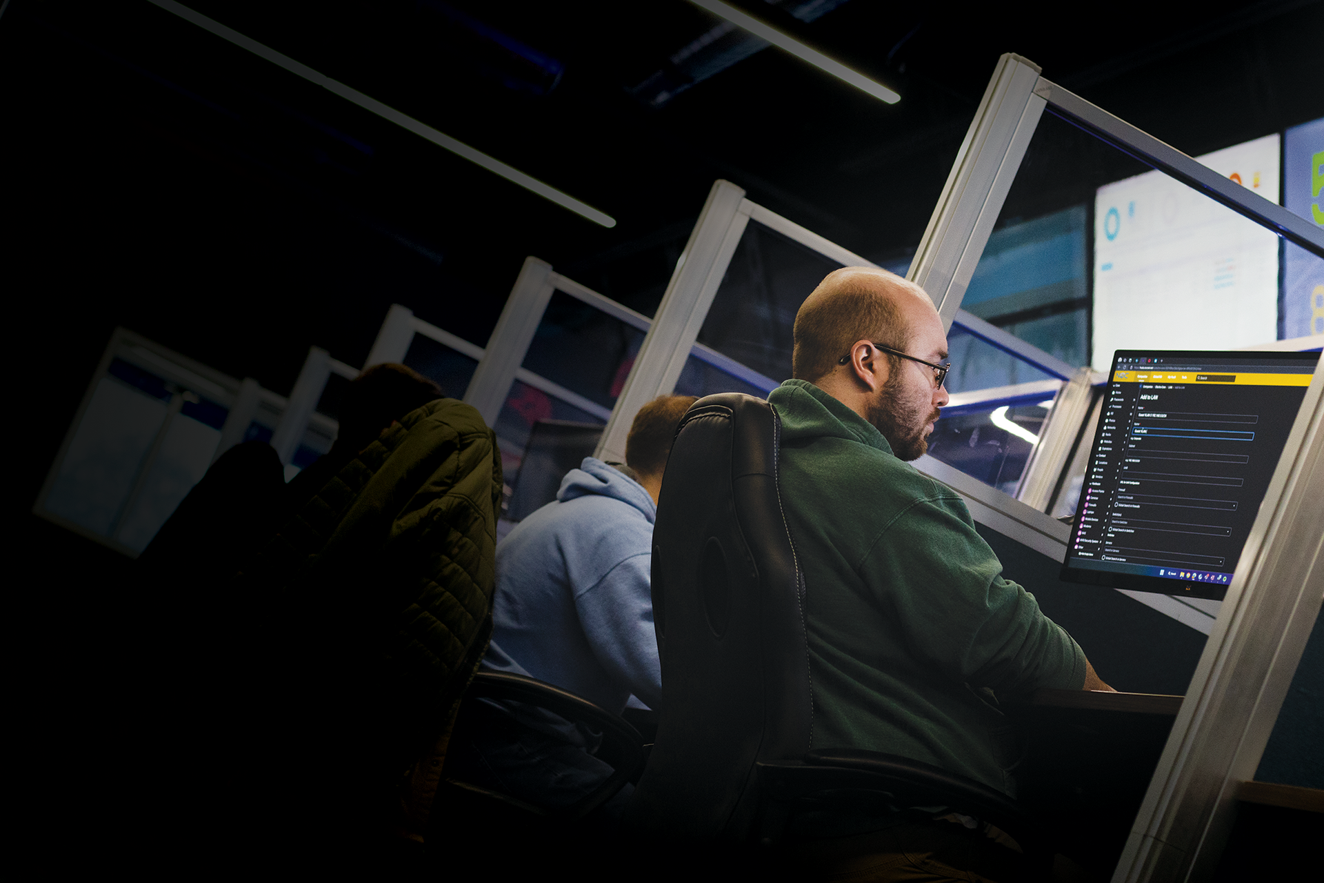 People working at computers in a dimly lit office, with code displayed on screens