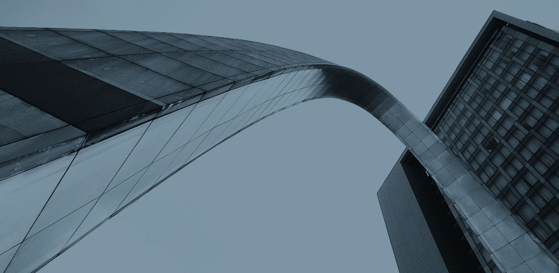 Low-angle shot of the Gateway Arch and a modern building in St. Louis, Missouri against a cloudy sky.