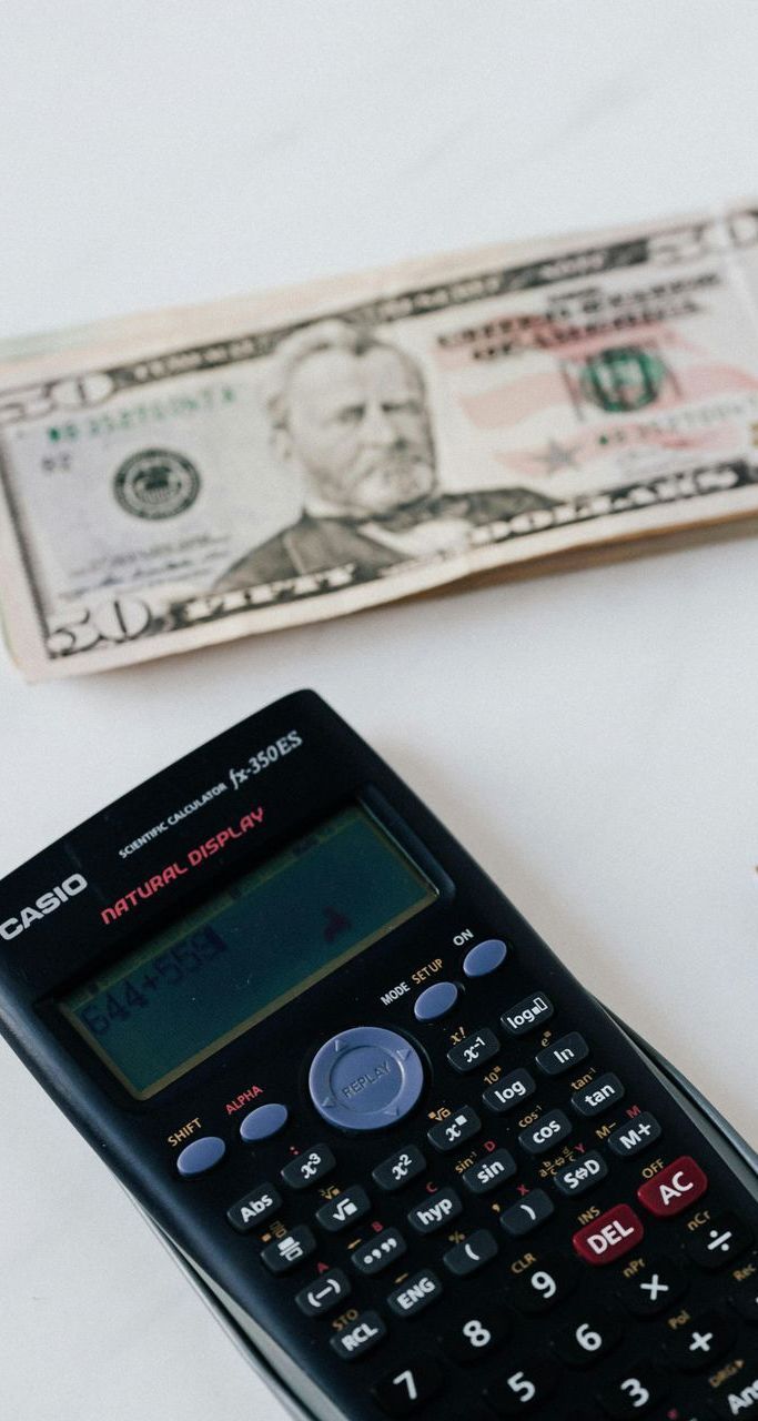 A calculator is sitting next to a stack of money.