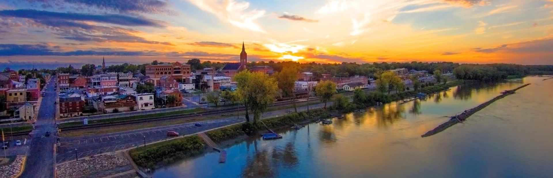 Sunset over a town with colorful buildings and a river. The sky is orange and blue.