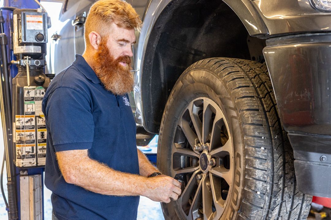 Mechanic with red beard tightening lug nuts on a tire in a repair shop.