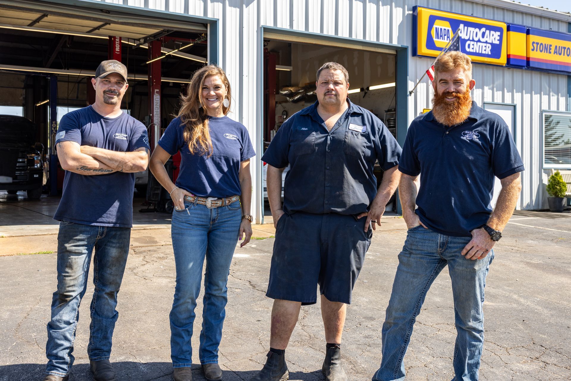 Four people pose in front of a NAPA AutoCare Center. They wear blue shirts, two in jeans, one in shorts. Red beard.