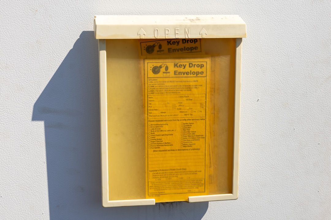 Yellow key drop box with instructions on a white wall.