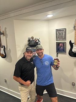 Two men are posing for a picture in a room with guitars on the wall.