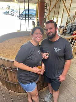 A man and a woman are standing next to each other in front of a large wooden barrel.