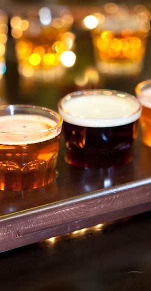 Three cups of beer are sitting on a wooden table.
