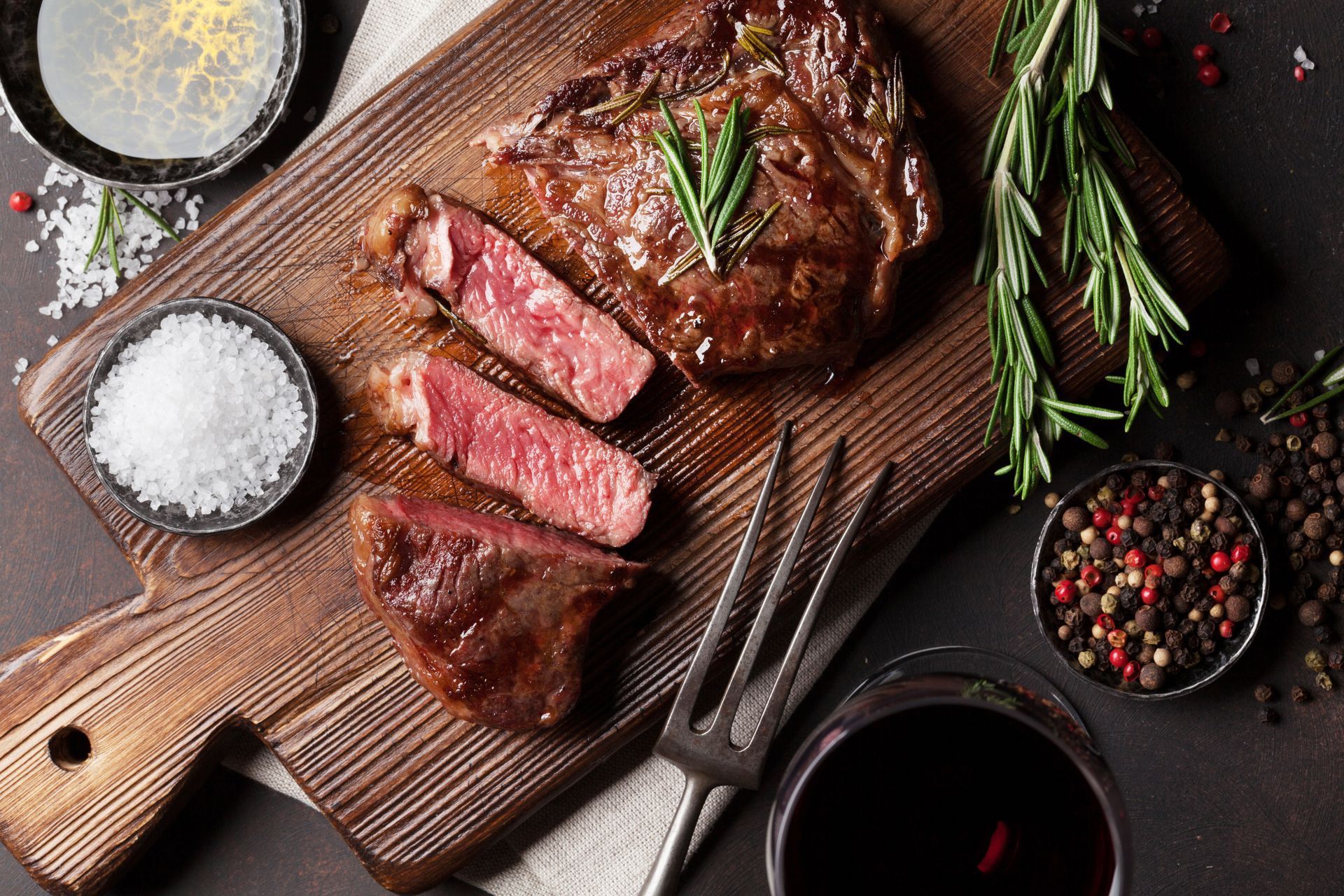 A steak is sitting on a wooden cutting board next to a glass of wine.