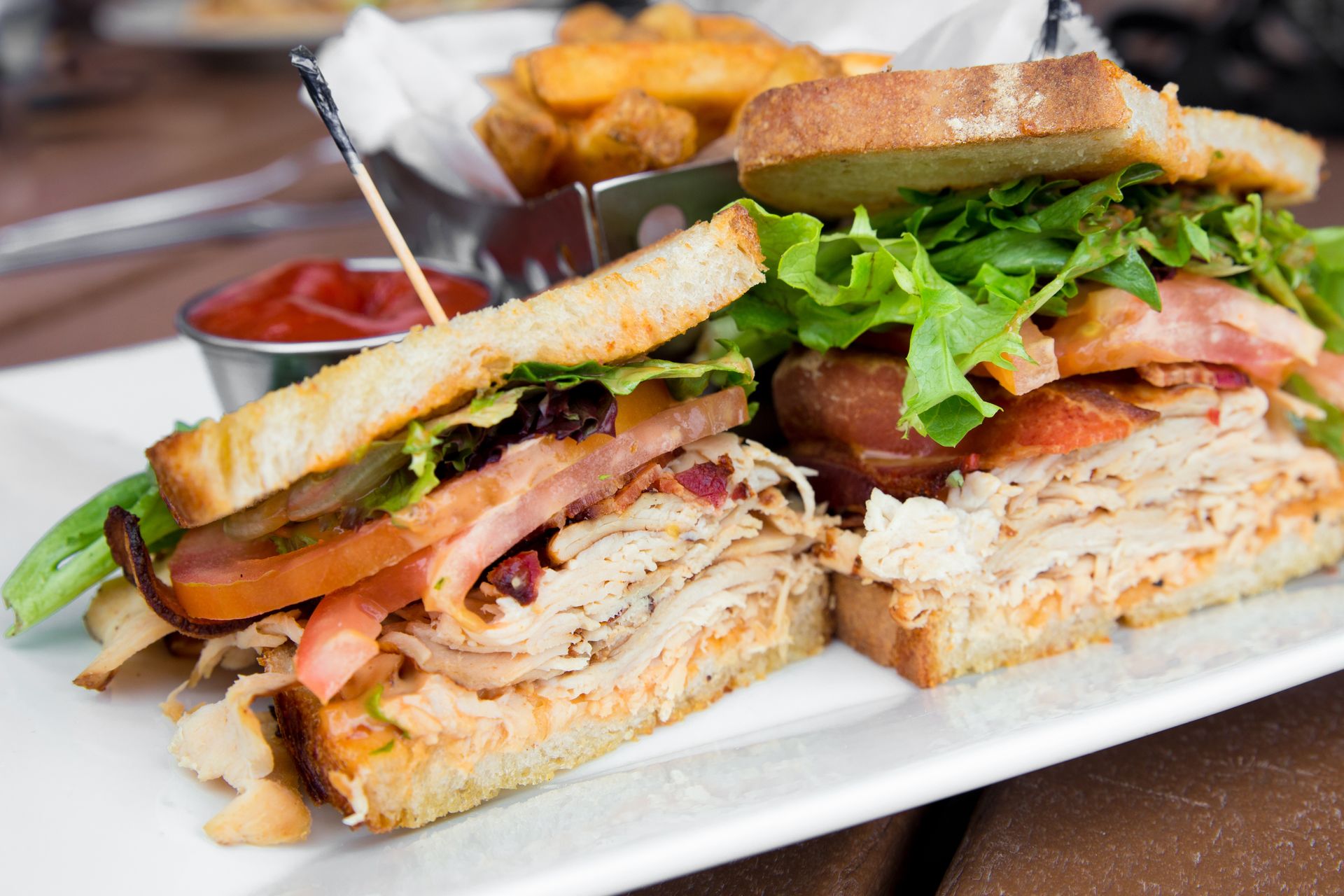 A club sandwich with turkey , bacon , lettuce and tomatoes on a white plate with french fries.