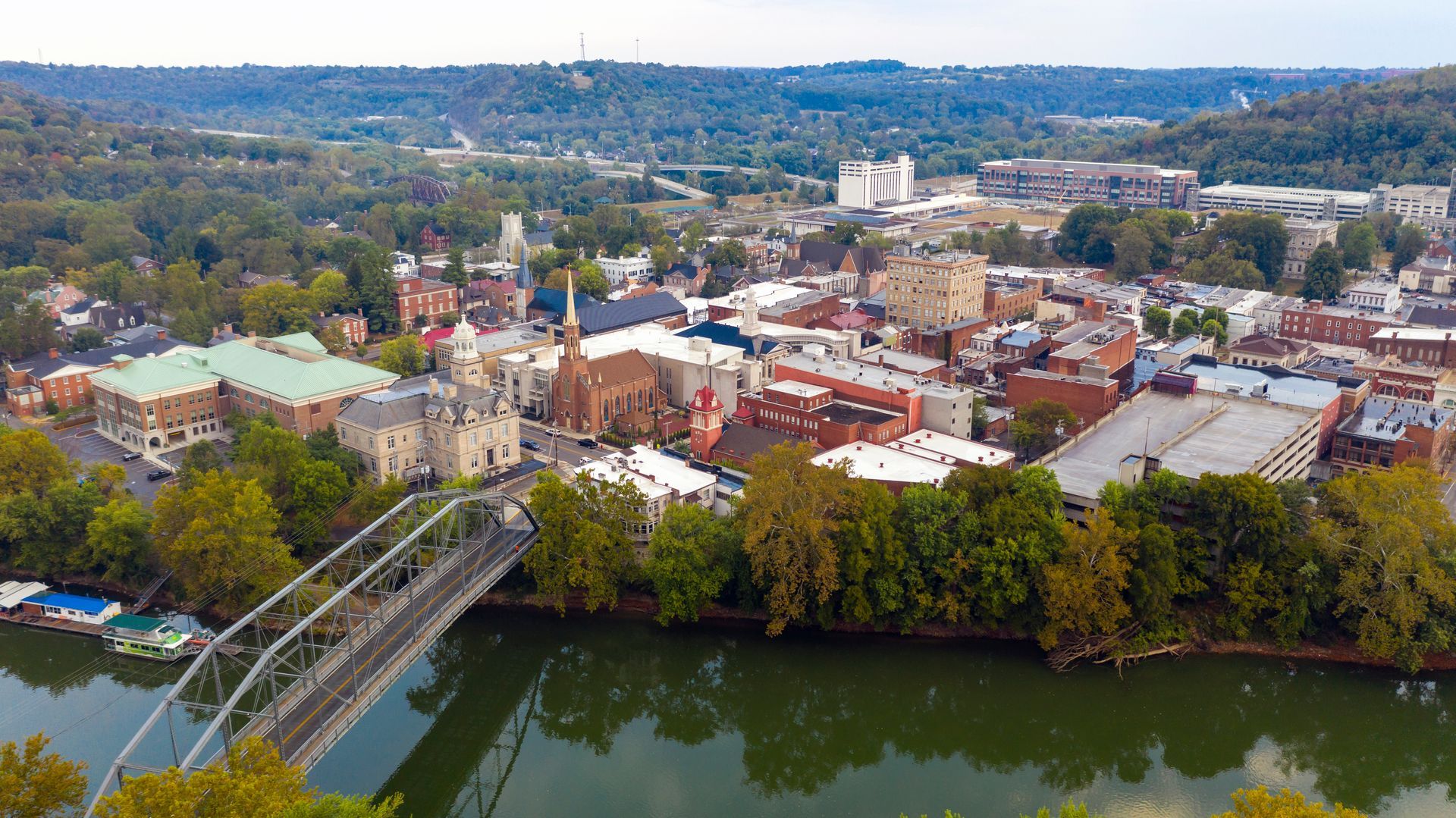 Aerial view of a town with buildings, trees, and a river with a bridge. Overcast day.