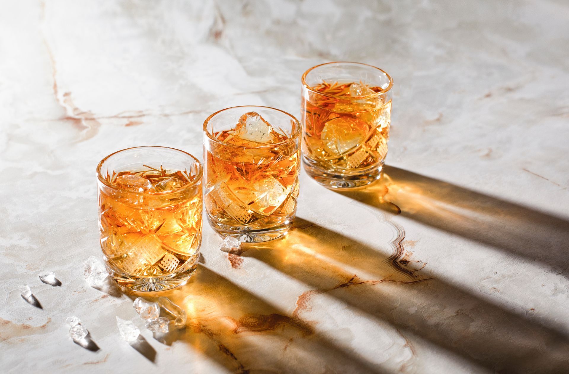 Three glasses of whiskey with ice on a table.