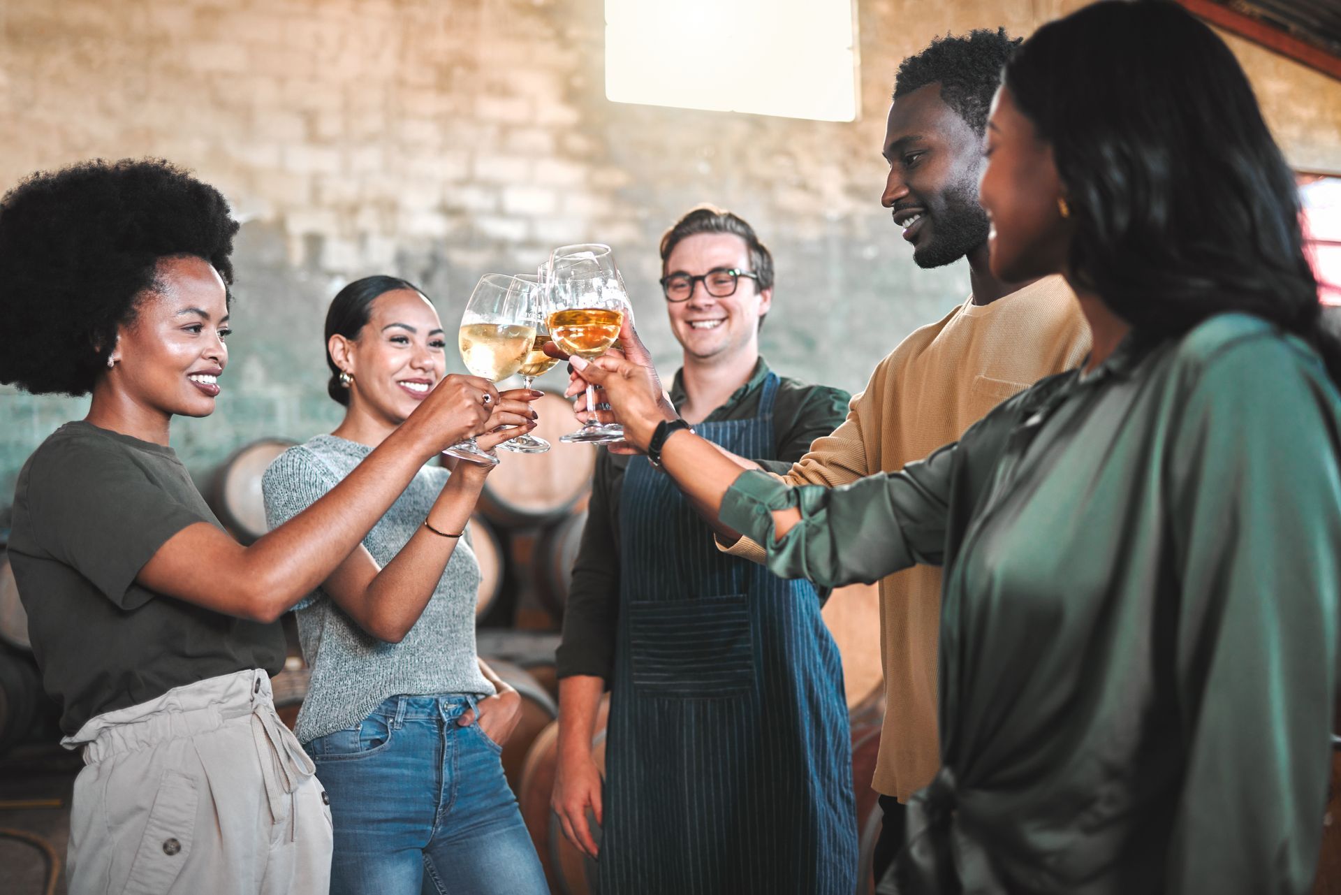 A group of people are toasting with wine glasses in a winery.