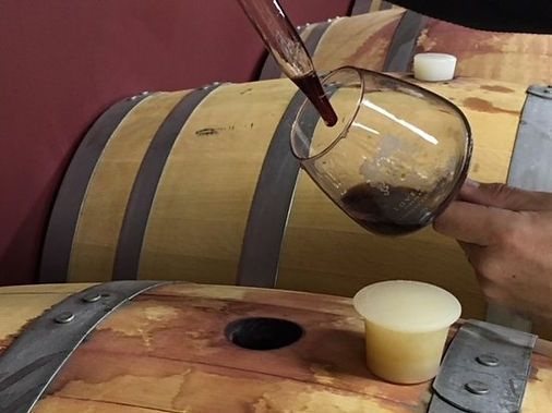 A glass of wine is being poured into a wooden barrel