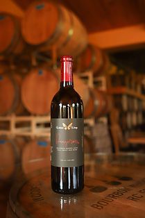 A bottle of red wine is sitting on top of a wooden barrel in a wine cellar.