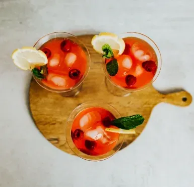Three craft cocktails garnished with lemon, mint, and berries