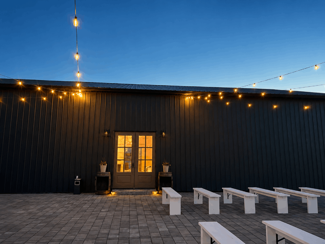 Bourbon Barrel Cottages black barn exterior at dusk with string lights and white ceremony benches
