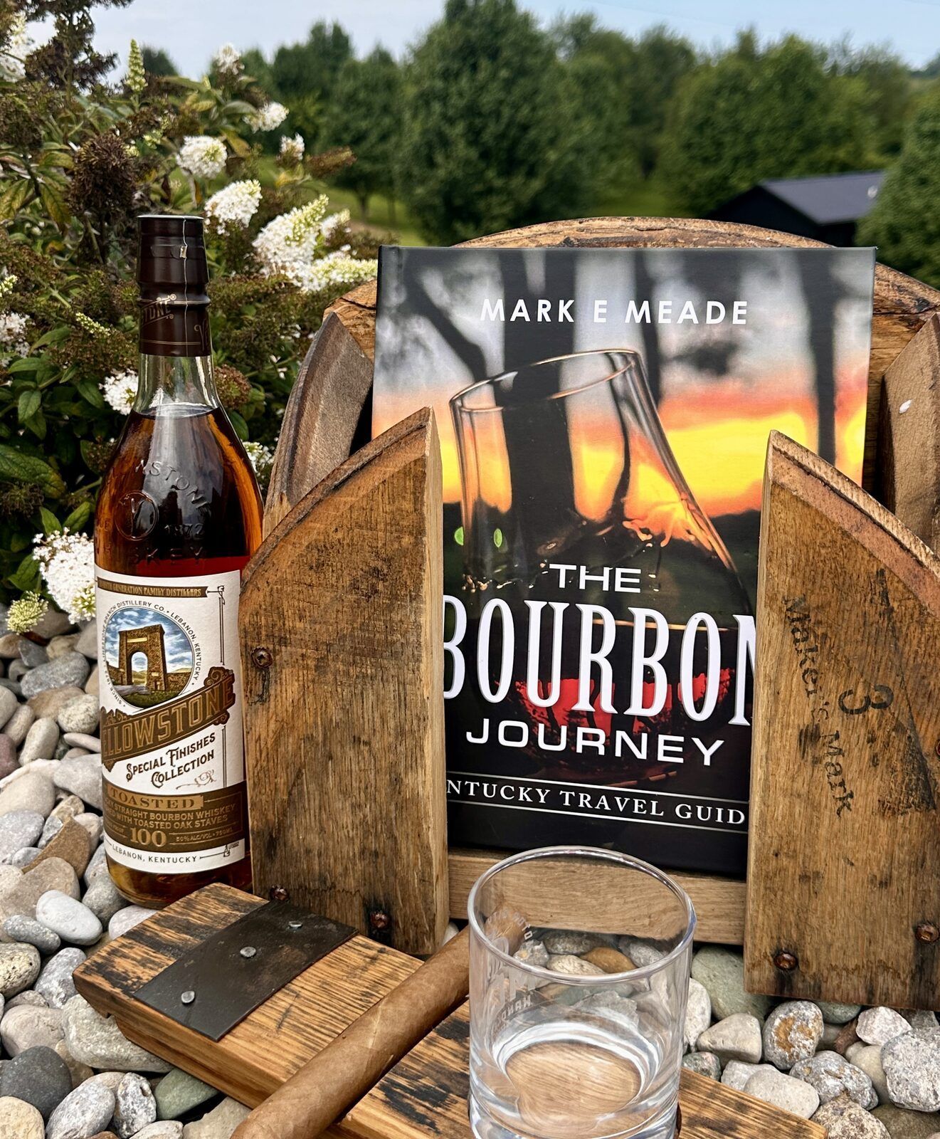 The Bourbon Journey travel guide, a bottle of Yellowstone bourbon, and a handcrafted barrel stave holder styled outdoors