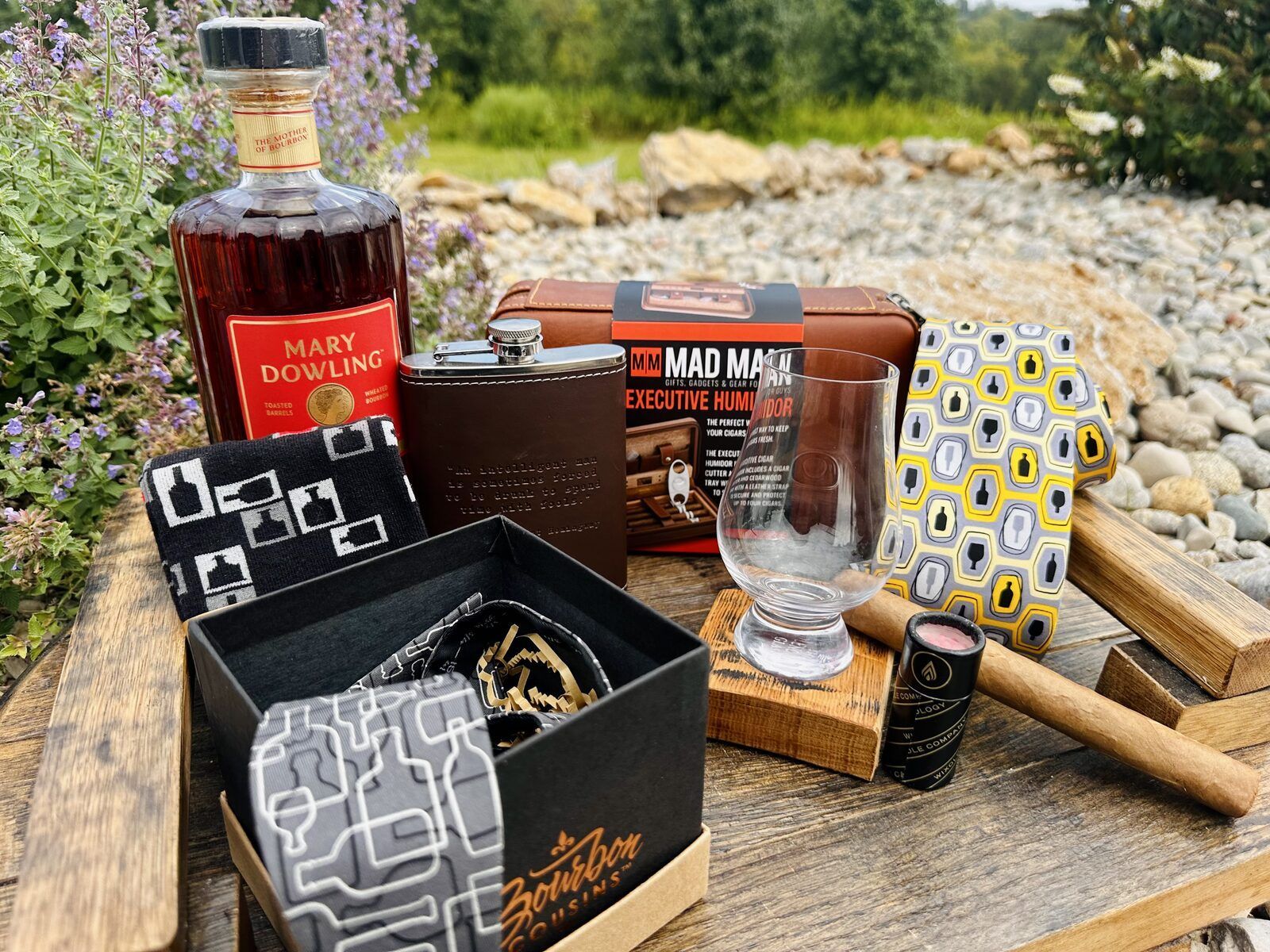Bourbon-print necktie, leather flask, cigar humidor set, and Glencairn glass styled on a barrel-stave tray