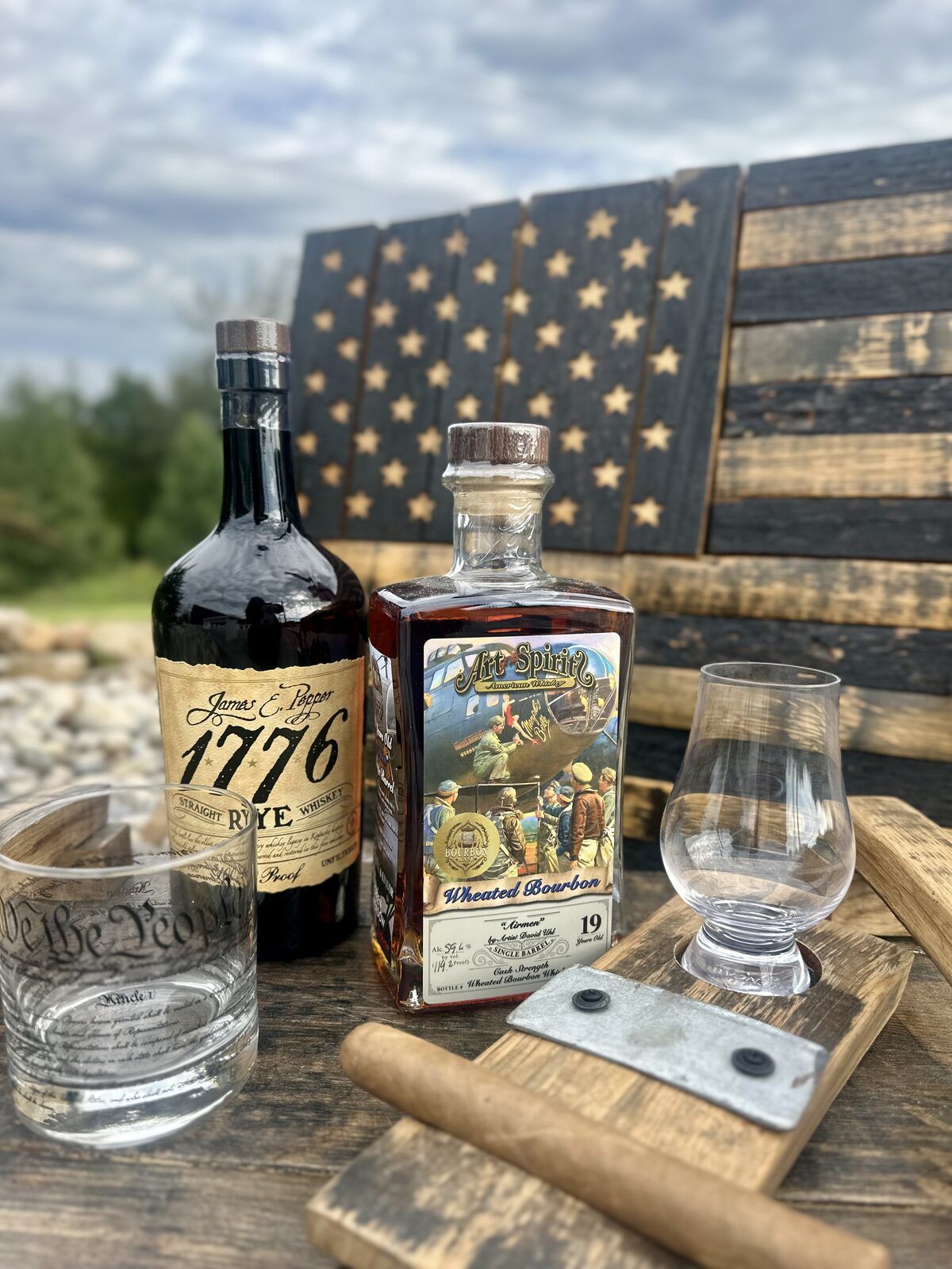 We the People bourbon rocks glass, Glencairn glass, and whiskey bottles styled in front of a handcrafted wooden American flag