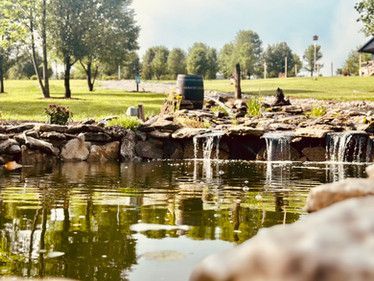 A pond with a waterfall in the middle of a park.