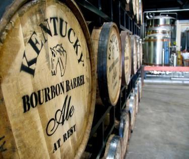 A row of kentucky bourbon barrels are lined up in a warehouse