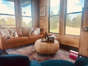 A living room with a brown couch , blue chairs , and a round ottoman.