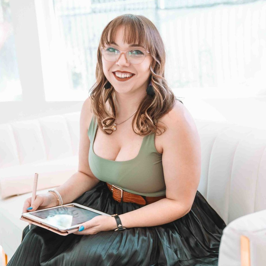 Woman sitting on a white couch, smiling and using a tablet in a bright room.