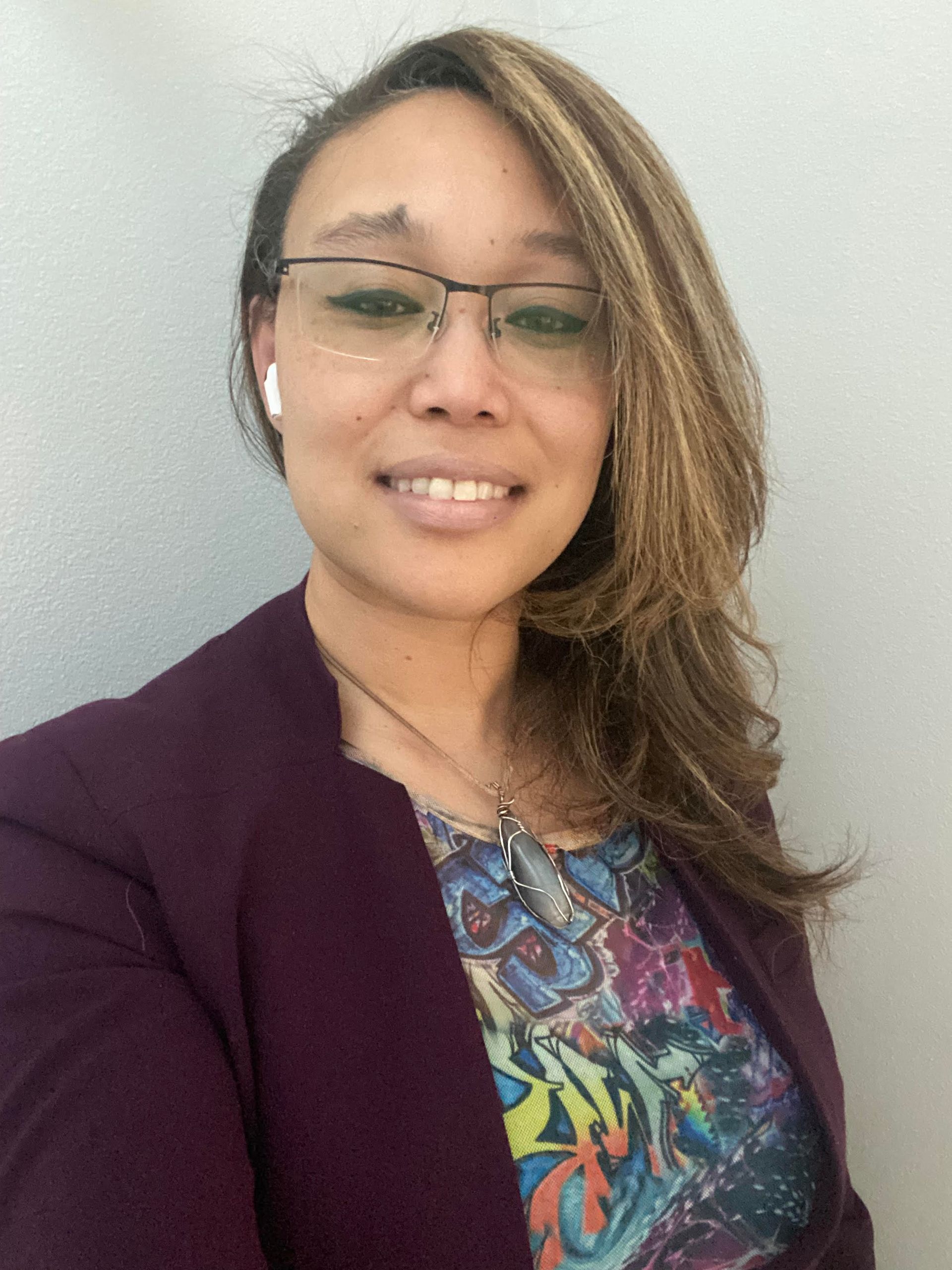 Woman wearing glasses and a purple blazer, smiling against a light gray background