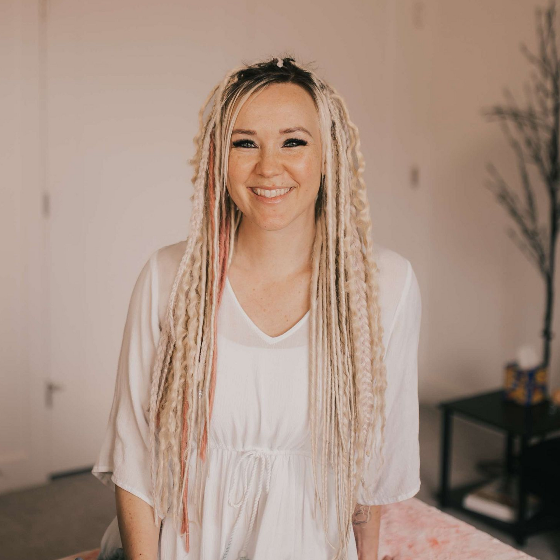 Smiling woman in a white dress with long braided hair standing indoors