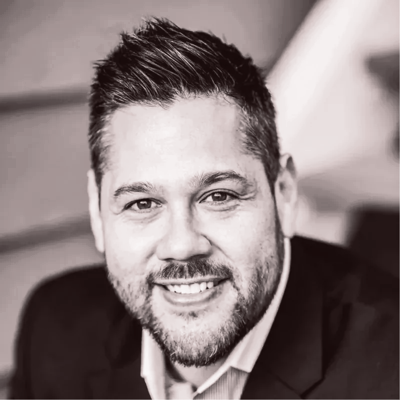 Smiling man in a dark blazer, shown in a black-and-white close-up portrait.