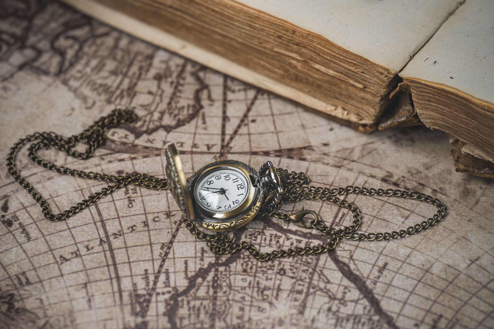 Vintage pocket watch on a chain resting on an old map beside an open book.