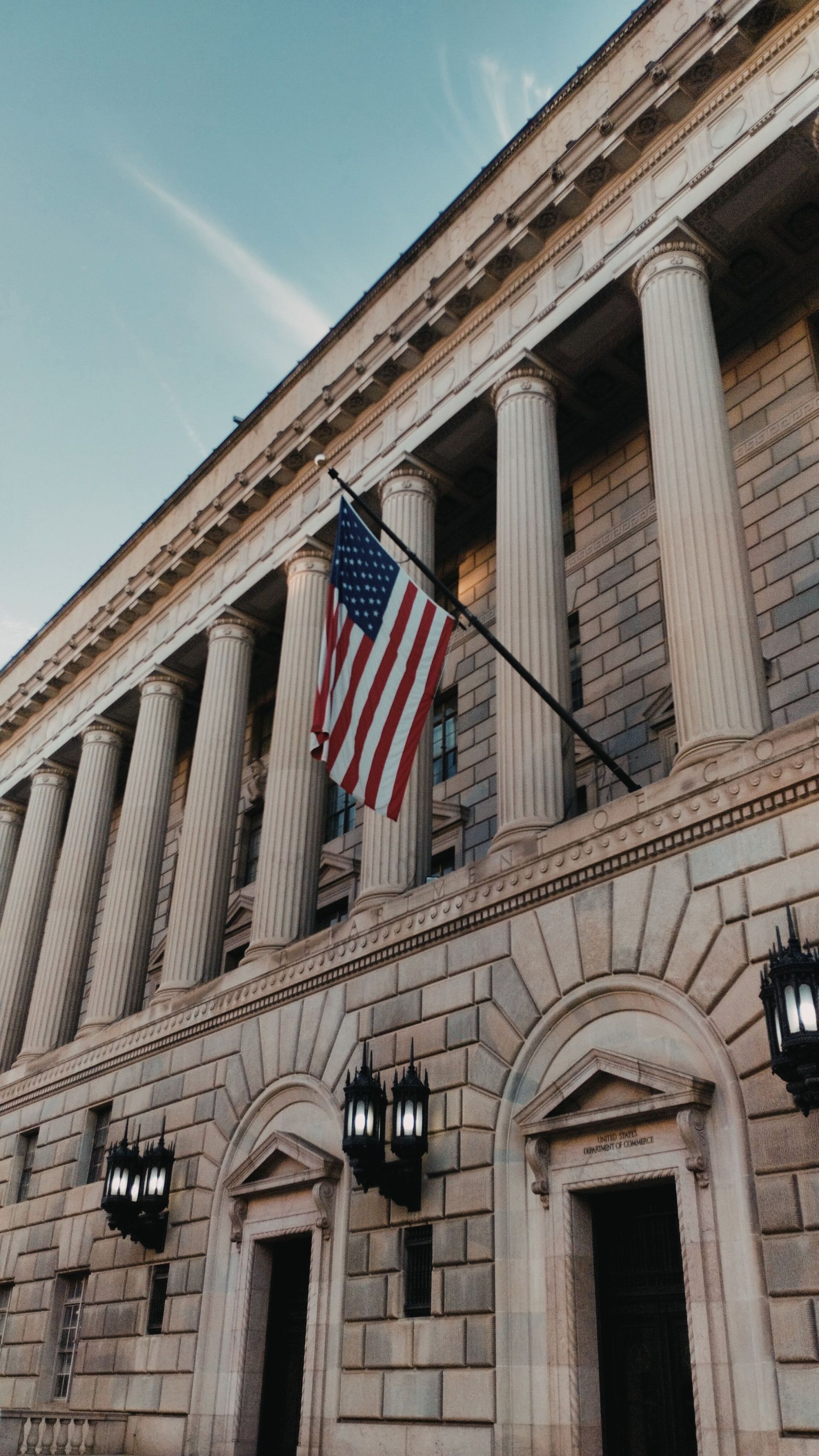 Stone civic building facade with tall columns and a hanging American flag