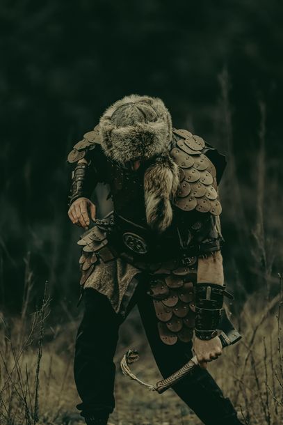 Armored medieval warrior wearing a fur hood, holding a sword in a dark forest