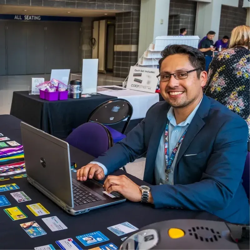 Man in a blue suit smiling at a laptop in a conference hall booth