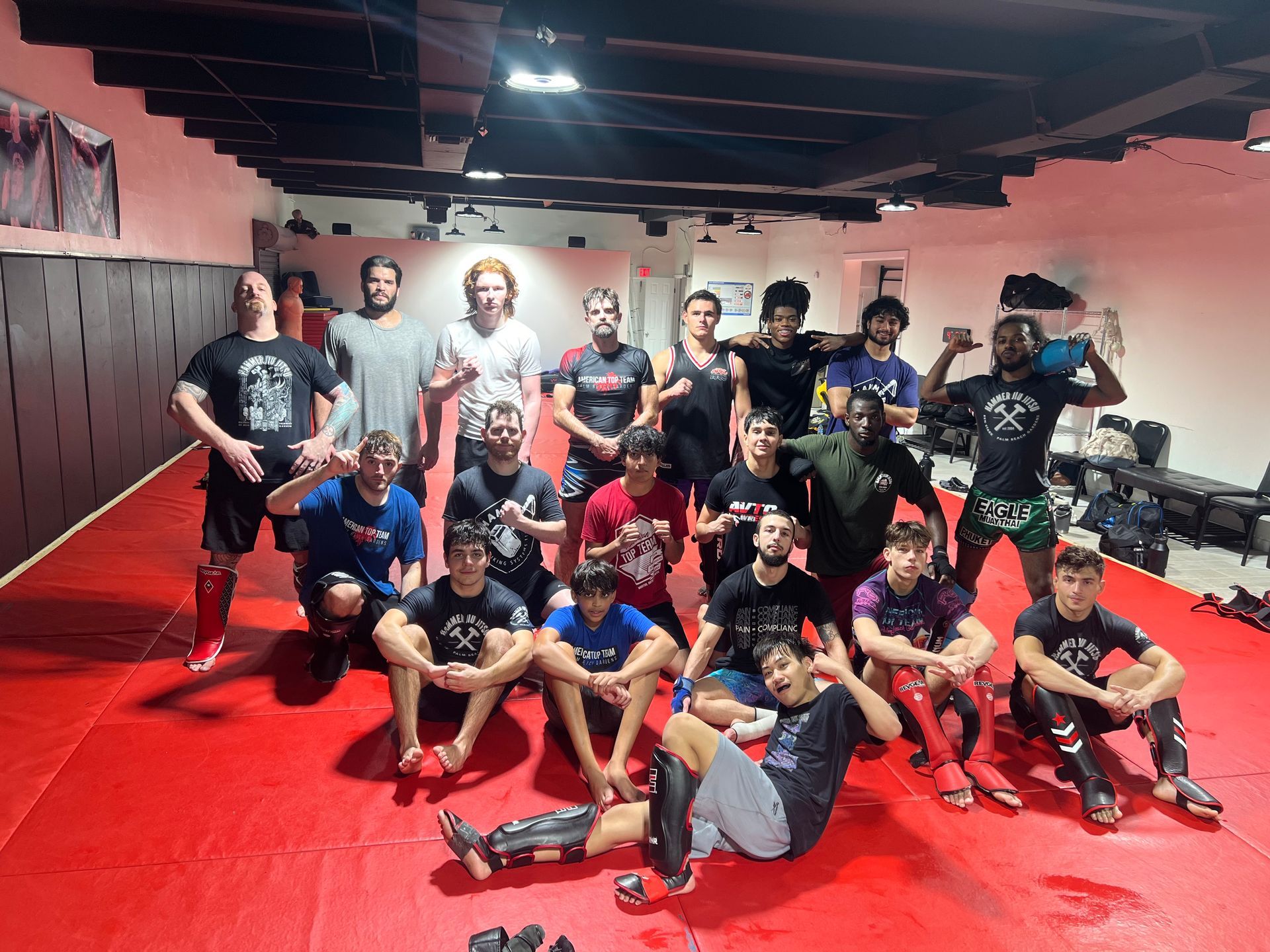 A group of people posing on a red matted floor in a gym, wearing athletic clothes and mixed martial arts gear.